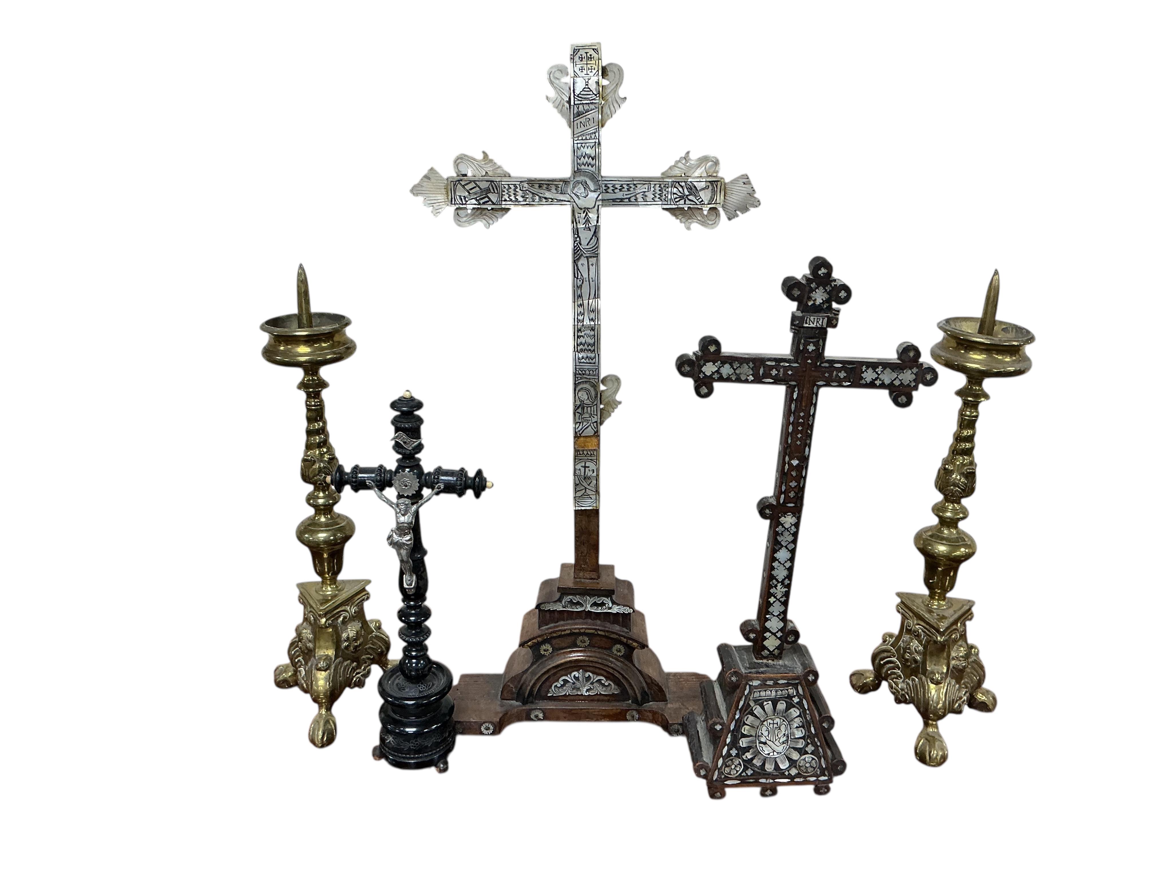 Two 19th century walnut and mother-of-pearl inlaid crucifixes and a German ebonised and white and metal mounted crucifix and a pair of Dutch or German brass tripod base cricket candlesticks, largest 56cm high (5)